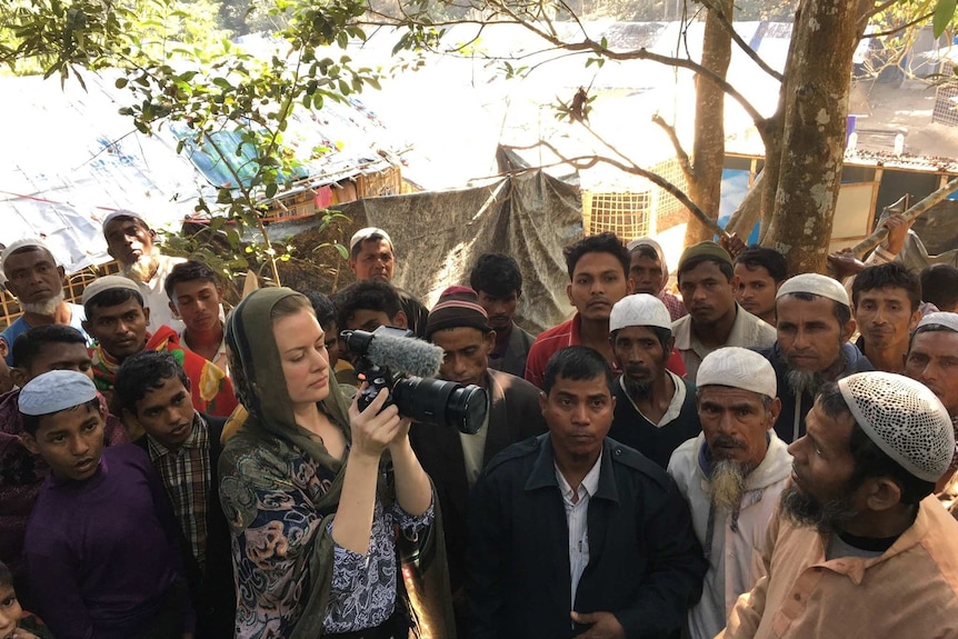 Heanue wearing headscarf filming men in refugee camp.