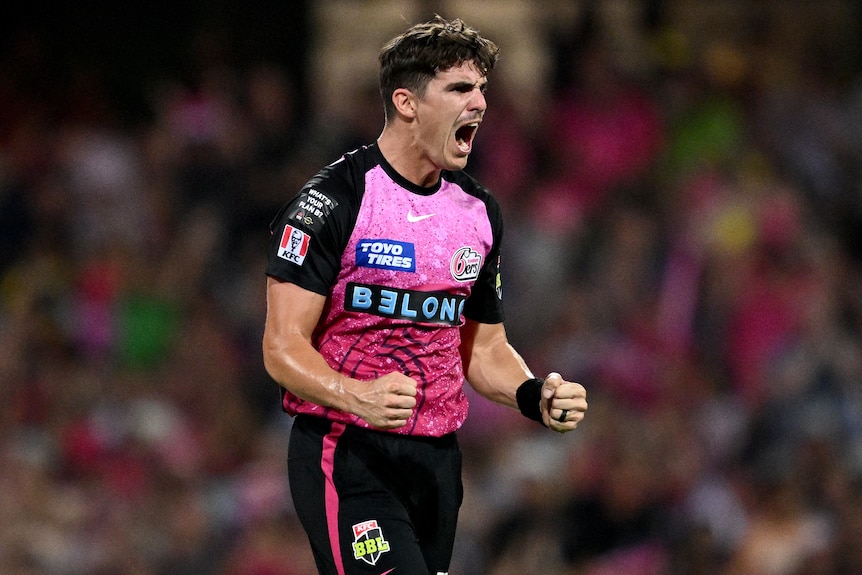 A man in a black and pink cricket uniform celebrates.