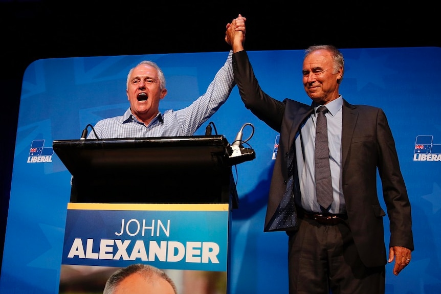 Prime Minister Malcolm Turnbull and John Alexander raise their arms celebrating Alexander's re-election
