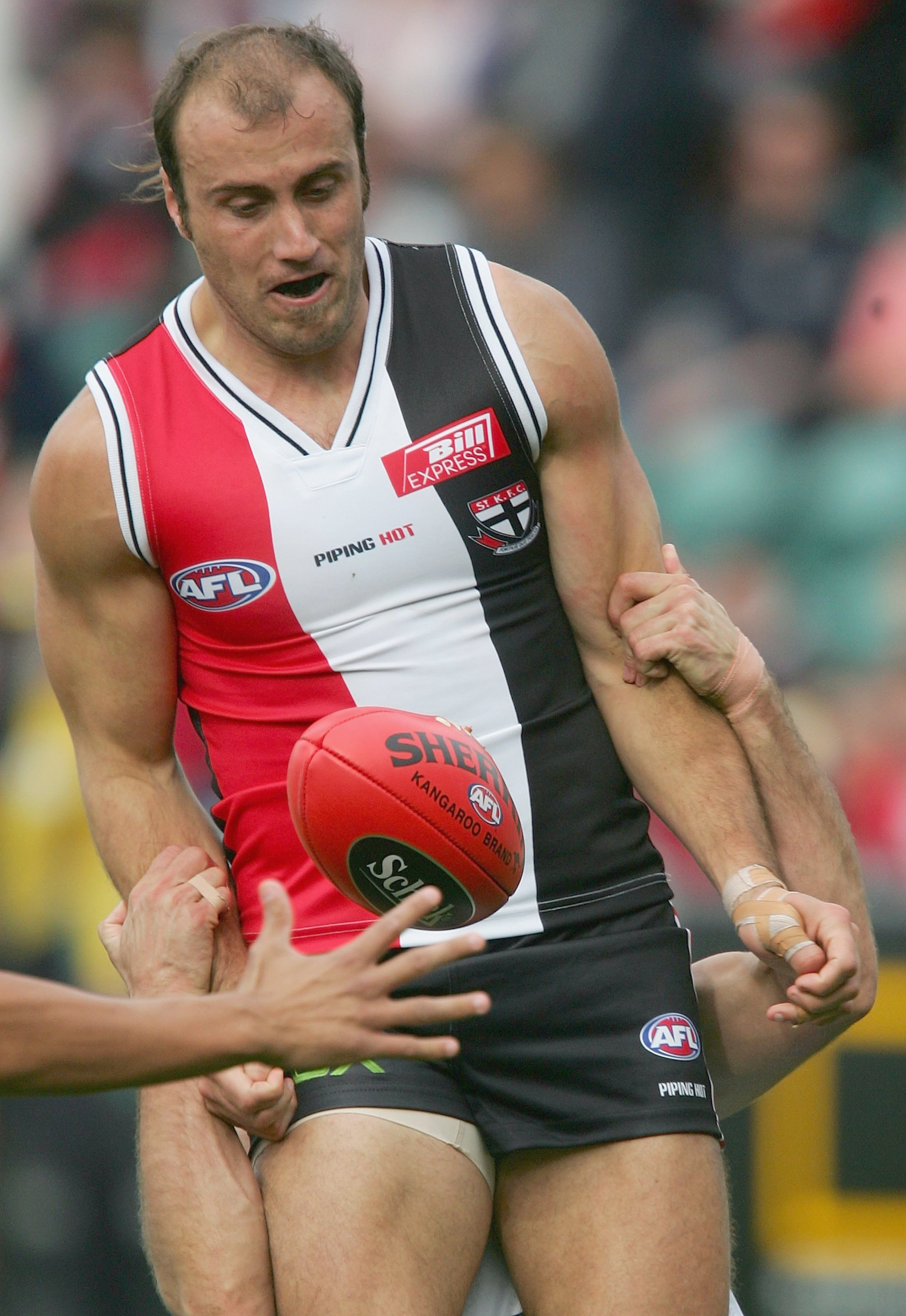 A St Kilda AFL player grimaces as his arms are held as he tries to mark the ball.
