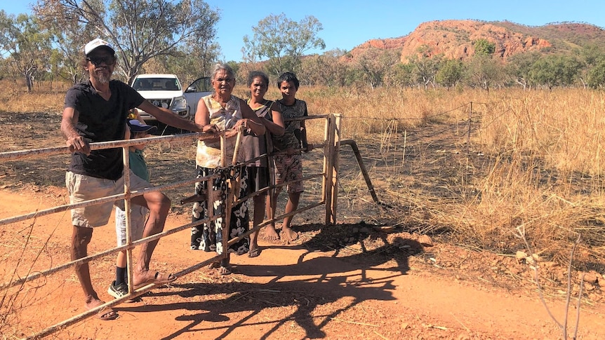 A man and a woman with their children standing behind a metal gate in a red, dusty landscape.