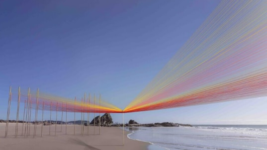 Artwork on a beach incorporating coloured string and 40 poles.  