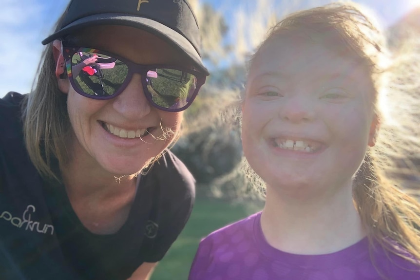 A mother and daughter smile at the camera with sun shining down. 