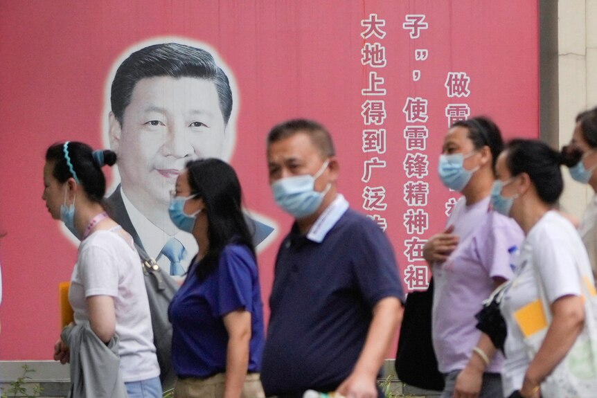 People wearing masks pass by portraits of Chinese President Xi Jinping.