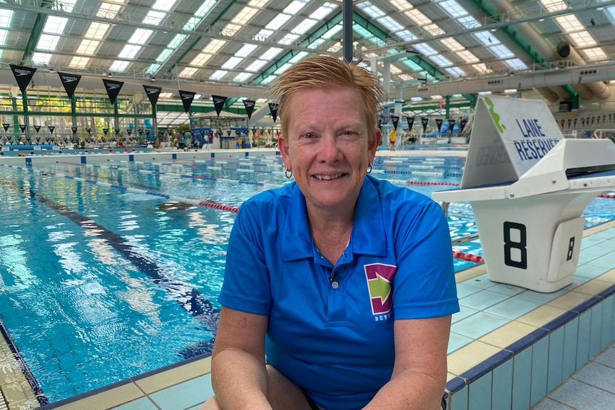 A woman smiles at the camera in front of a swimming pool.