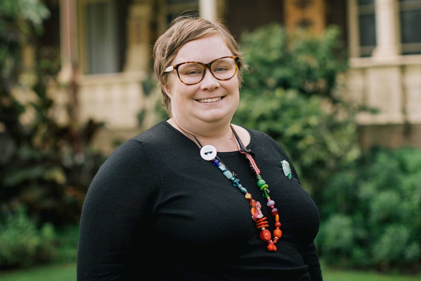 A woman with glasses and dressed in black stands in front of a historic building.