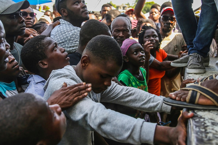 A teenage boy cries as he looks up from a dense crowd to a truck where sacks of rice are being handed out.