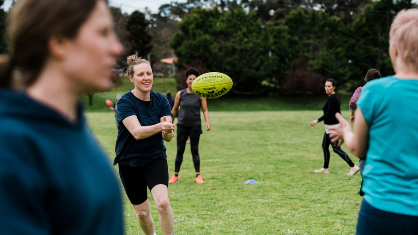 Women in dark active wear handballing a football to her teammate