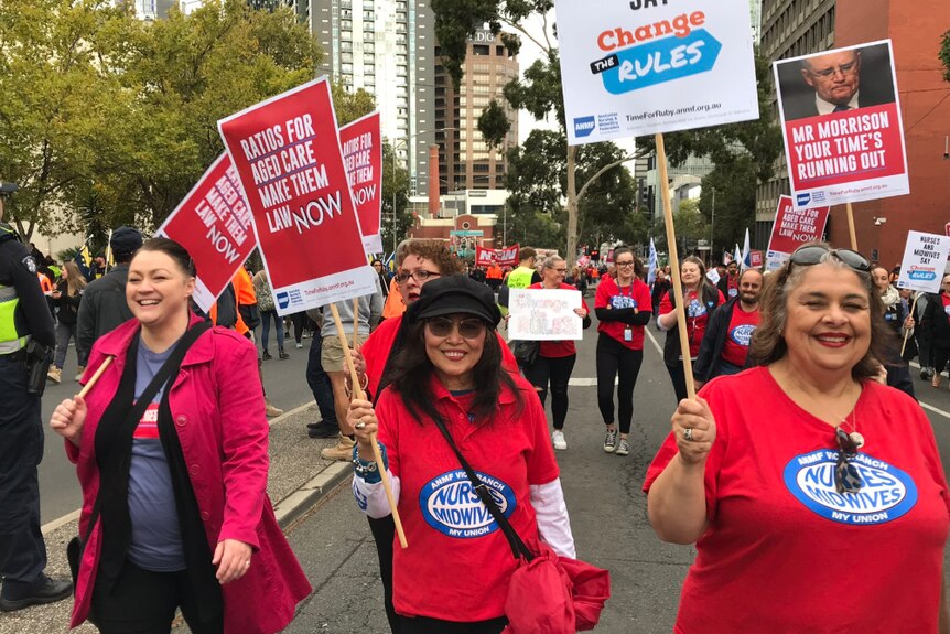 Women wearing red shirts carry signs reading 'ratios for aged care make them law now'.