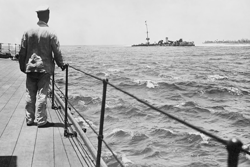 Man stands on deck looking at a ship