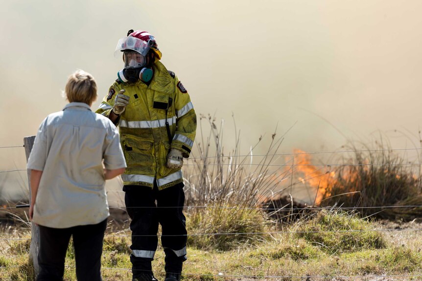 A woman and firefighter talk close to a small blaze in the background