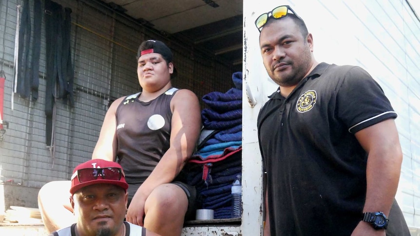 Three removalists stand at the back an open removal truck