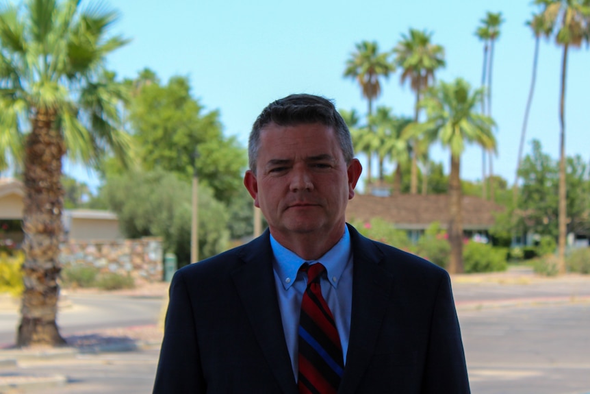 A man in a suit poses for a portrait in front of palm trees and sunshine
