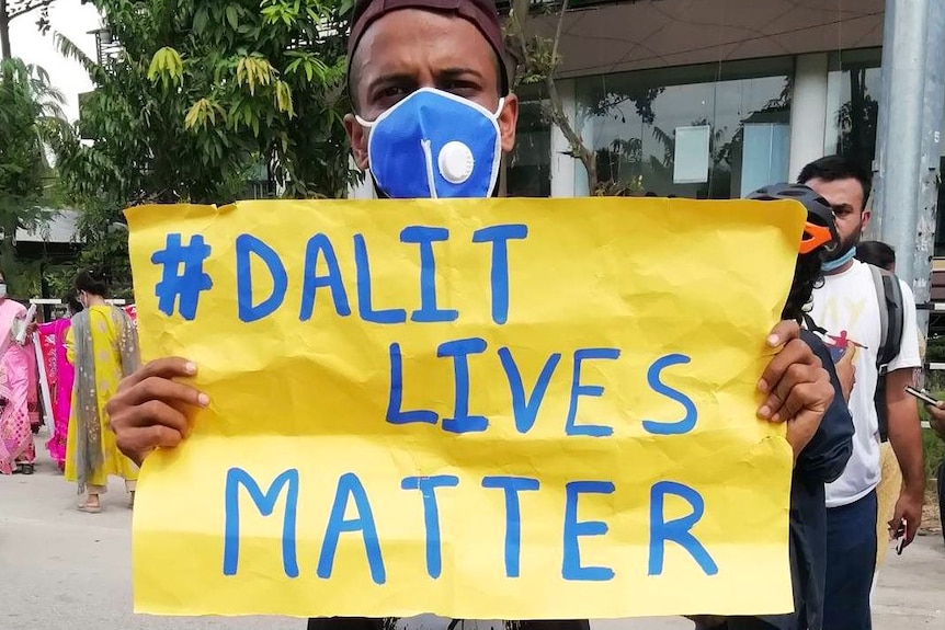 A man wearing a facemask holds a sign saying "# Dalit Lives Matter".