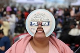 A person with a paper plate over their face which reads 2024 solar eclipse nyc. 