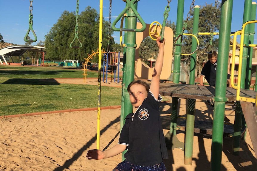Mackenzie Cook swings on monkey bars in a playground.