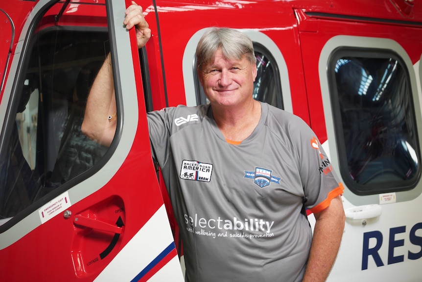 A man smiles and leans against the door of a red rescue helicopter 