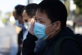 A side-on shot of a man wearing a face mask while talking on a mobile phone.