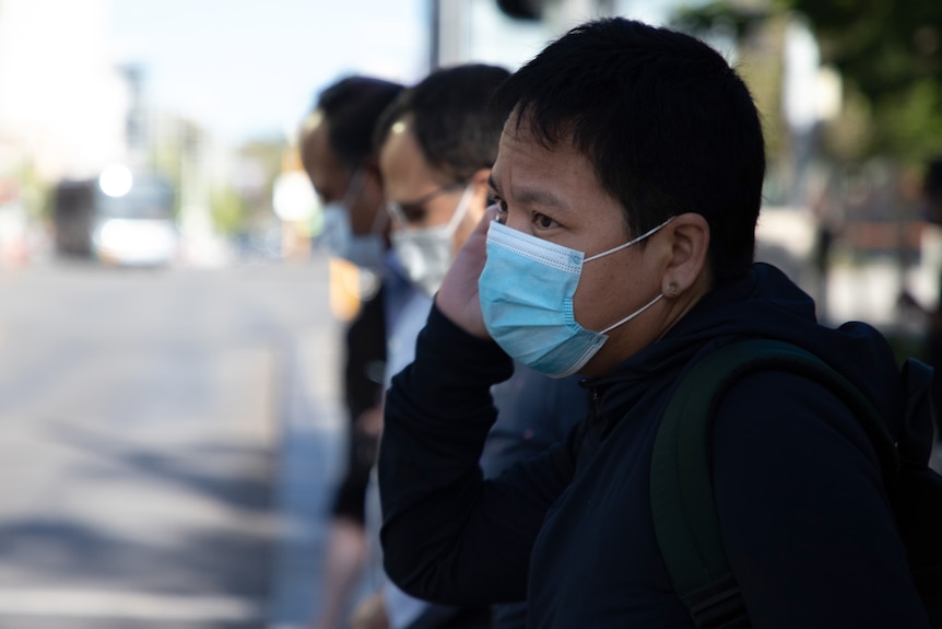 A side-on shot of a man wearing a face mask while talking on a mobile phone.