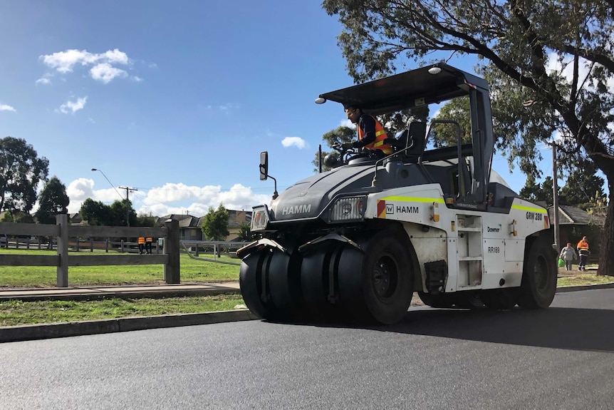 A construction worker drives a steamroller on a road .