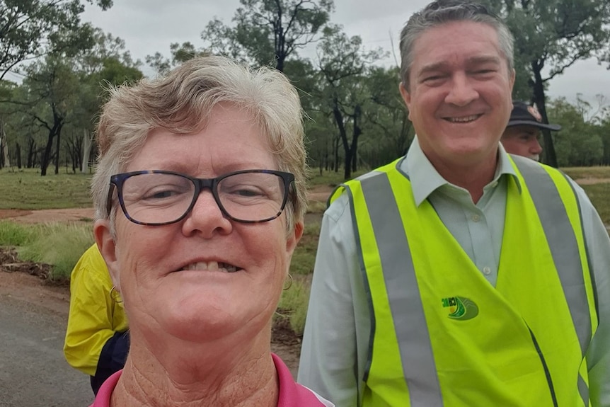 Sandy Willcott smiles taking a selfie with Kerry Hayes, wearing high visability vest, trees behind.