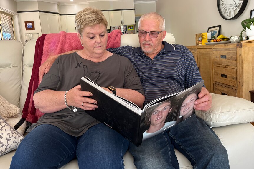A man and a woman sitting on a couch looking at a photo album.