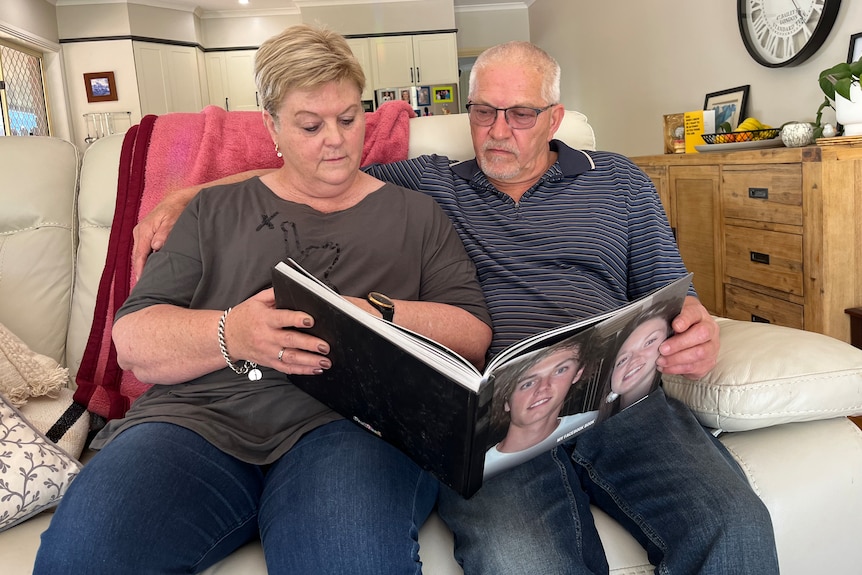 A man and a woman sitting on a couch looking at a photo album.