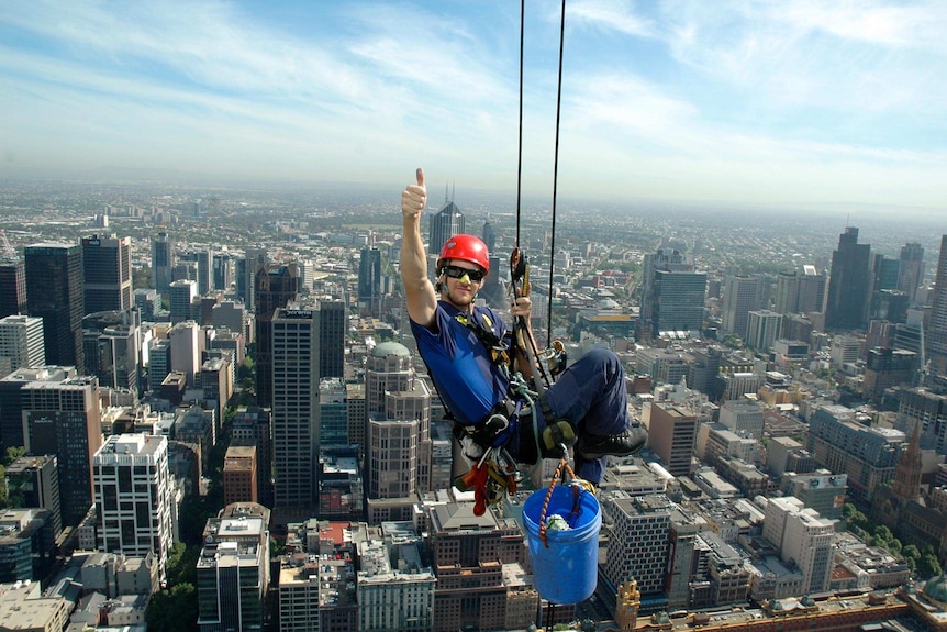 A man abseils with a vista of Melbourne behind him