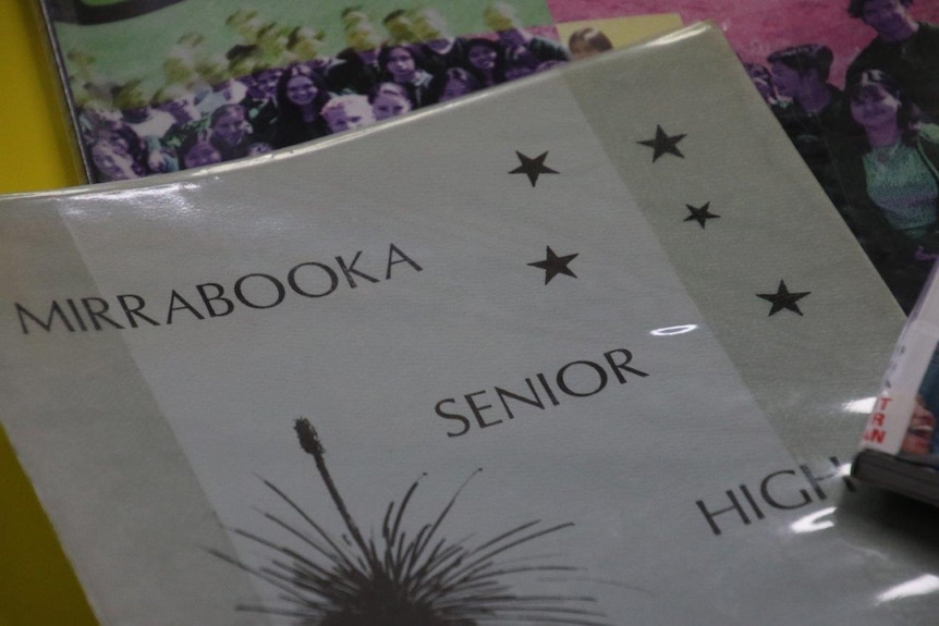 A close up of a grey school year book, that reads 'Mirrabooka Senior High', with stars and a cartoon grass tree on it.