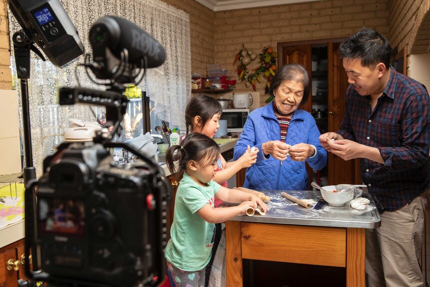 Great grandmother Ann Poon making dumplings in the kitchen with her family, with camera gear in the foreground.