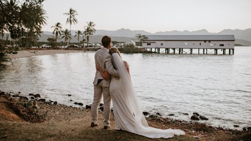 Couple in wedding clothes gazing out over water to Sugar Wharf in Port Douglas
