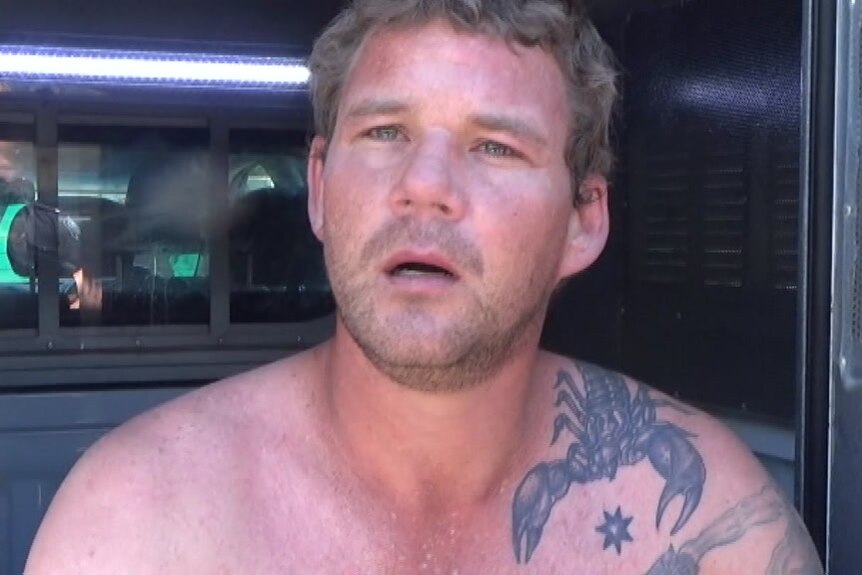 A man with tattoos and no shirt in the back of a police wagon
