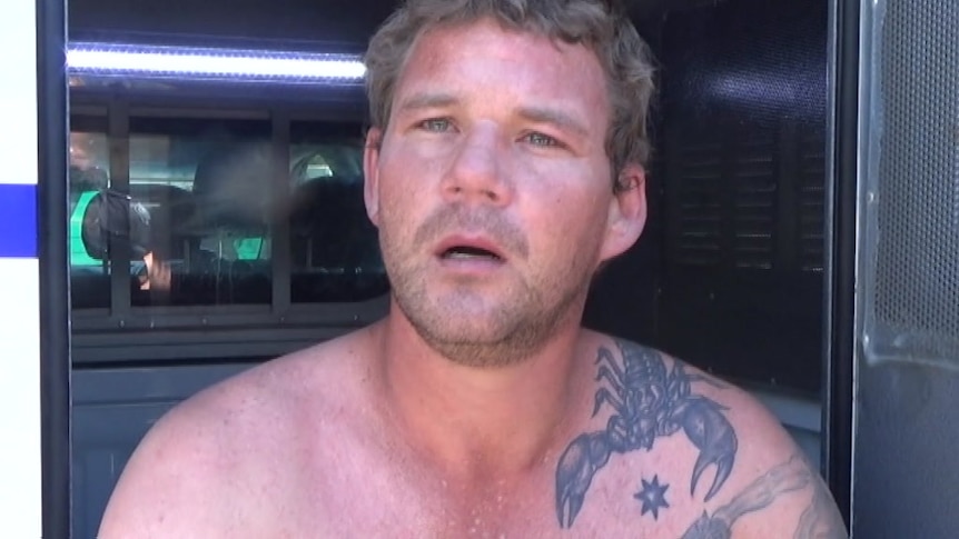 A man with tattoos and no shirt in the back of a police wagon