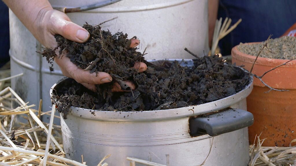 Hand holding dark compost over a pot.