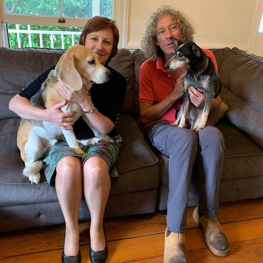 A man and woman sit on a couch each holding a dog.