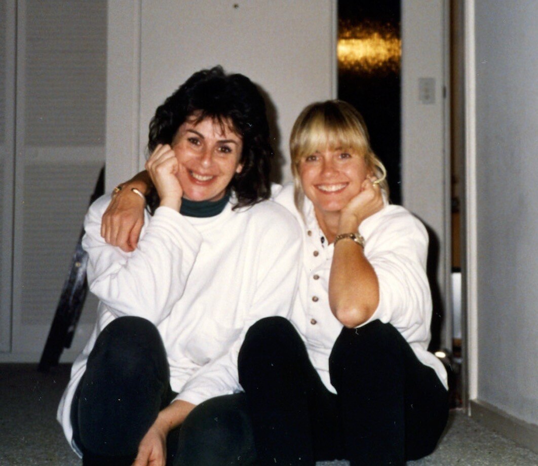 Two smiling women, one dark-haired and the other blonde.