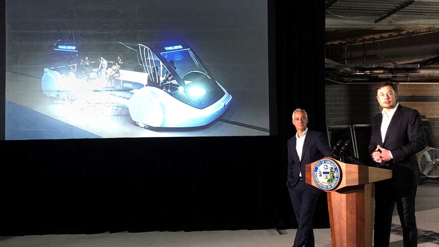 Elon Musk standing next to Chicago Mayor Rahm Emanuel with a projection of his commuter plan behind them.