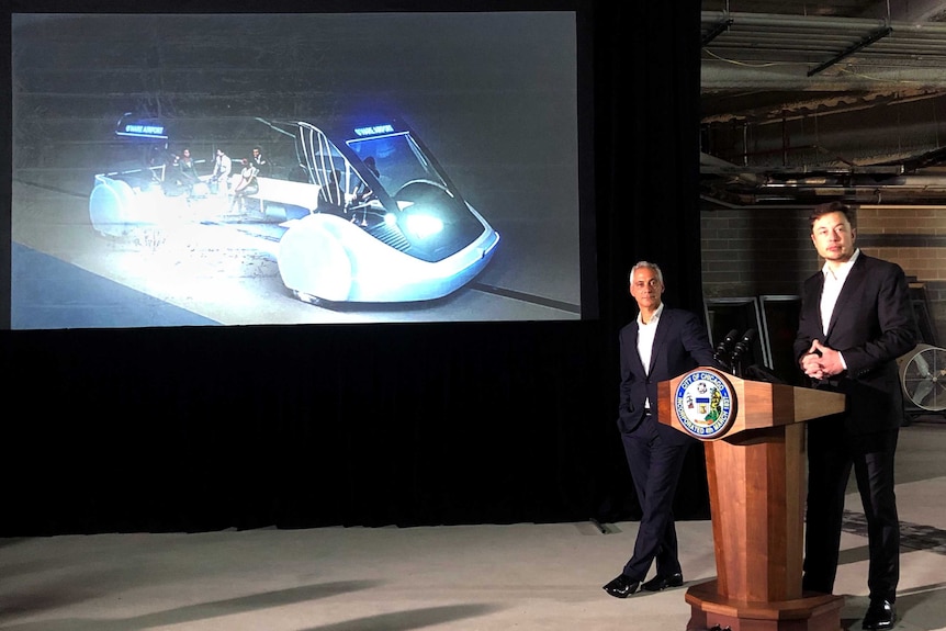 Elon Musk standing next to Chicago Mayor Rahm Emanuel with a projection of his commuter plan behind them.