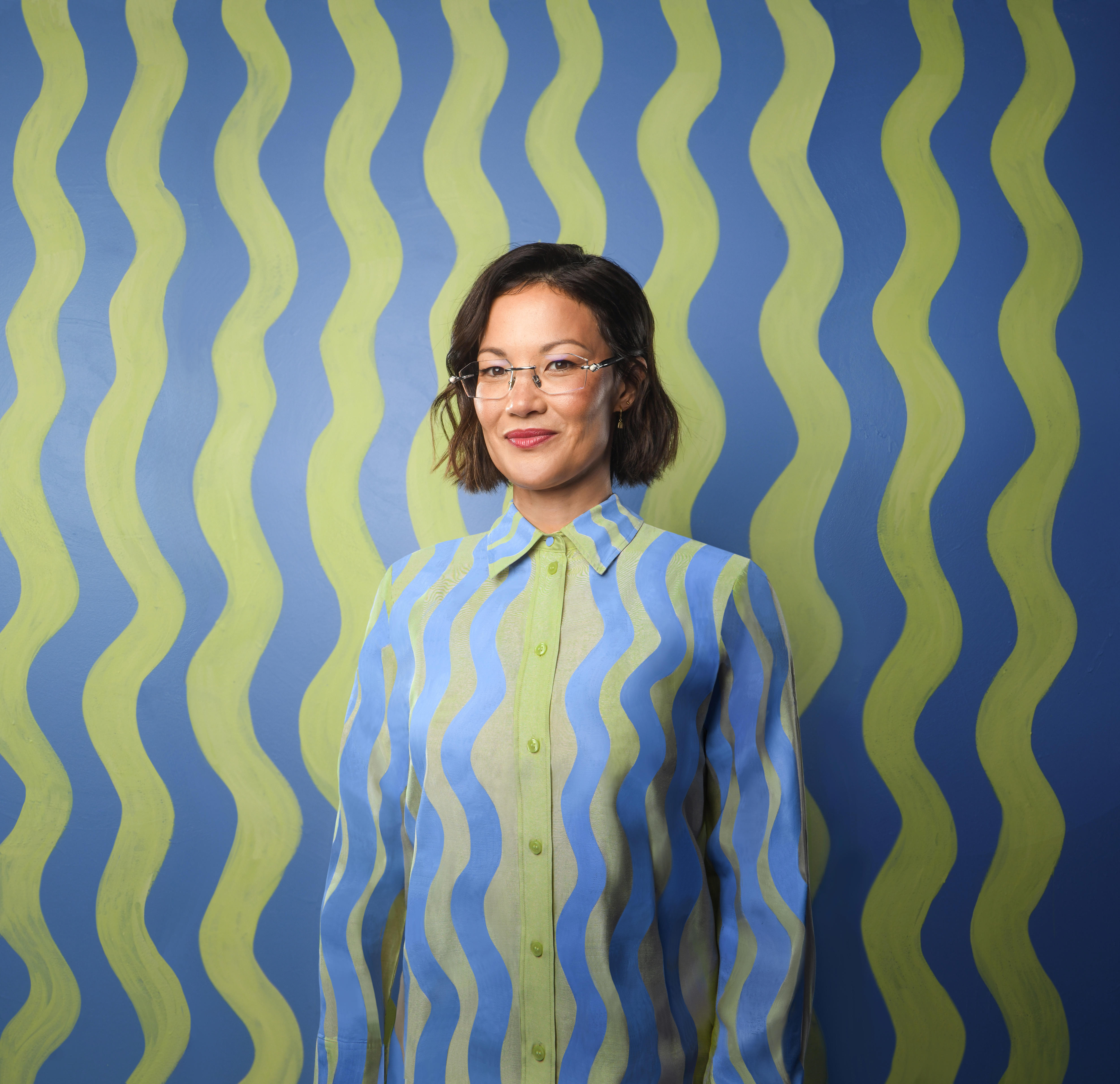 Comedian Lizzy Hoo stadning infront of a striped background,