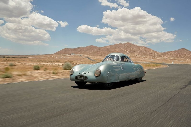 A metallic blue sportscar drives in the desert.