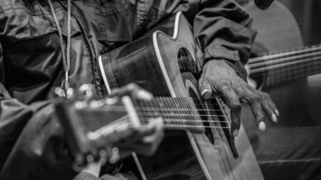 A black and white photographic close up of the hands of Dr G Yunupingu on his guitar