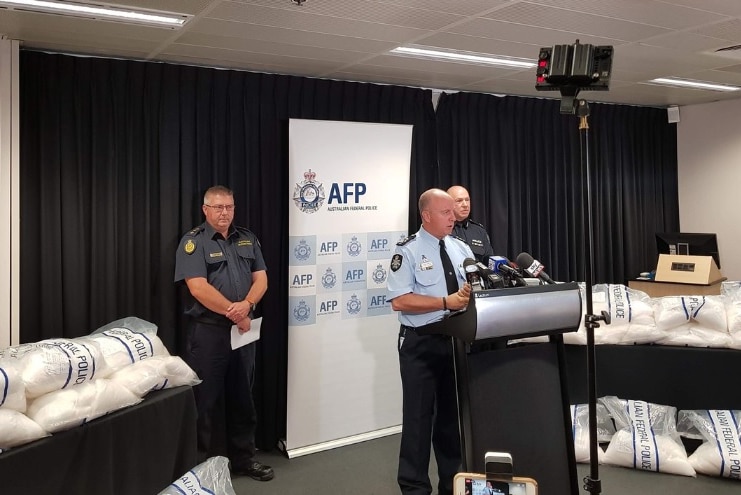 Police talk about a shipment of ice which is on tables near them.