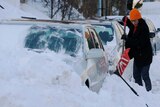 A woman digs out her car which has been buried in snow.