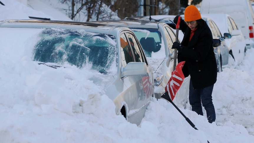 A woman digs out her car which has been buried in snow.