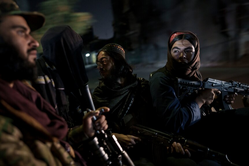 Four Taliban fighters ride in the back of a car in the darnkess, holding assault rifles