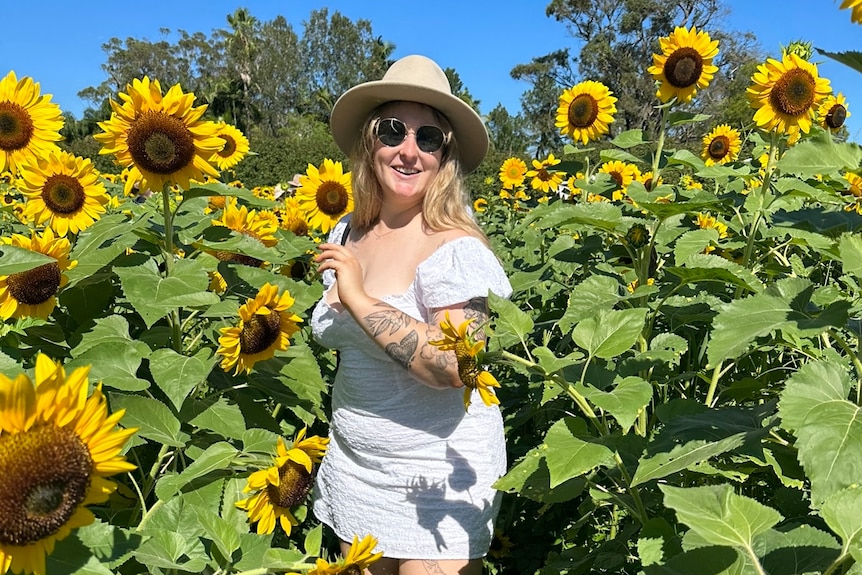 A young woman in a dress frolics in a field of sunflowers.