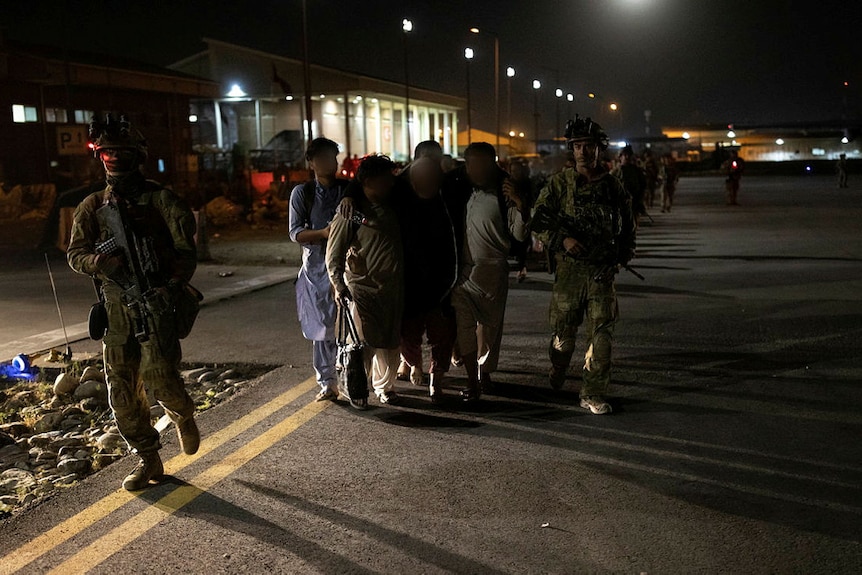 Two Australian soldiers escort a group of people on a road at night.