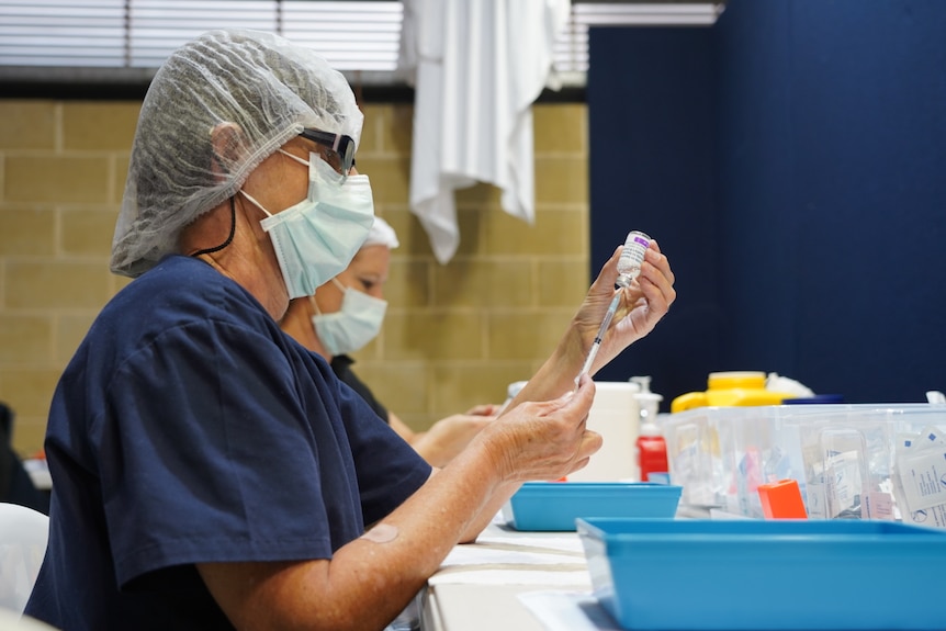 A health worker wearing a cap and mask prepares a COVID vaccine.