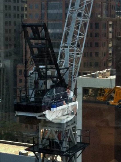 A crane driver without safety equipment sleeps on a ledge