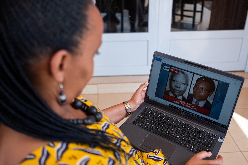 Rwandan genocide survivor looks at a laptop with pictures of Rwandan genocide figure Felicien Kabuga.